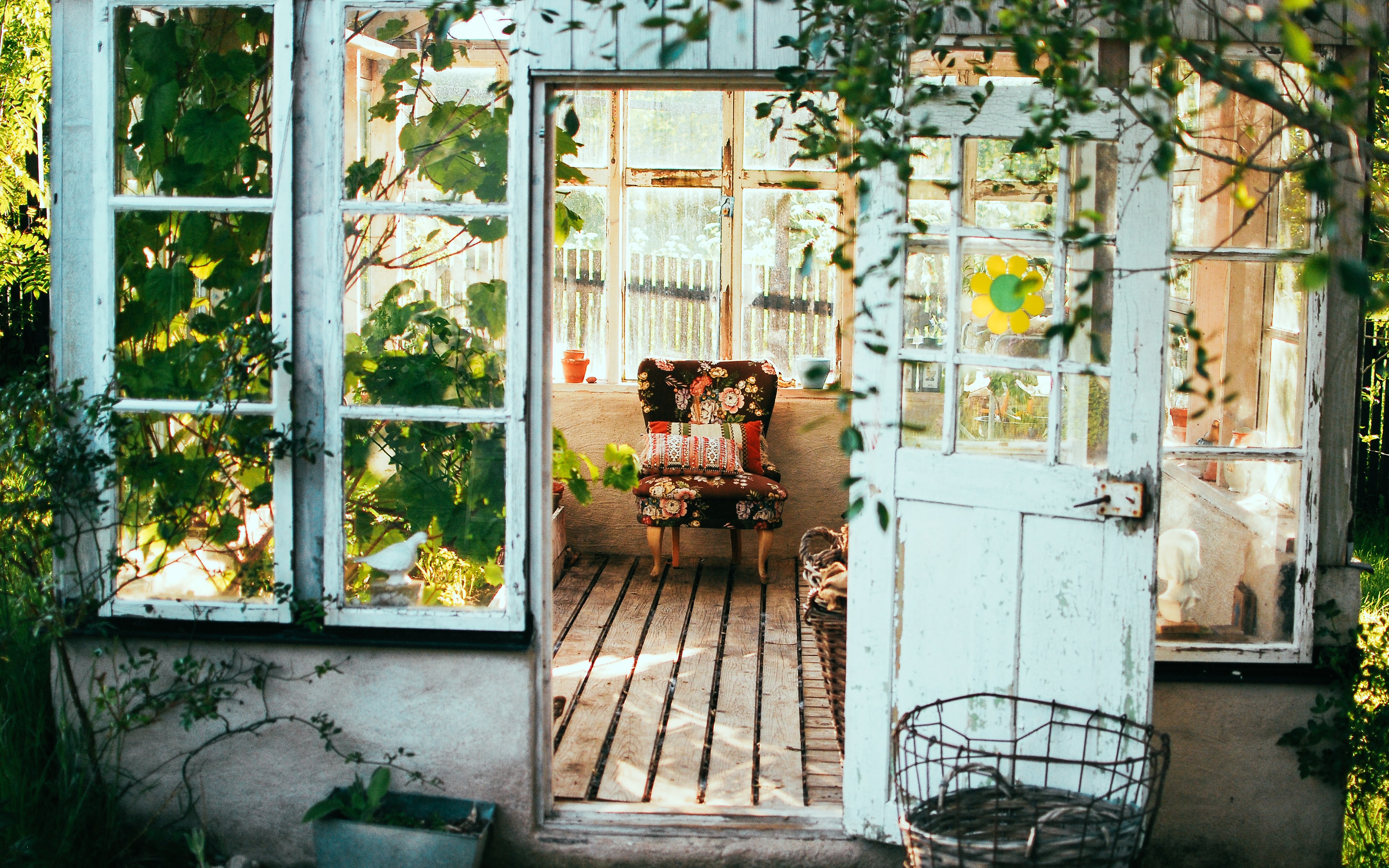 Image of open door to porch with inviting sitting chair, surrounded by plants.