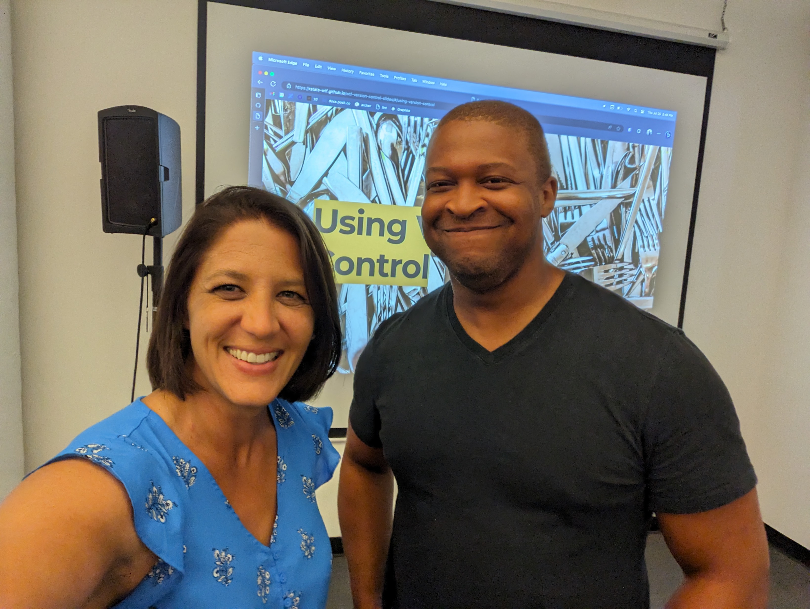 Shannon and David stand in front of a projected slide that has an image of a disarry of silver forks, knives and spoons with the title "Using... control" shown - "version" is blocked by David's head.